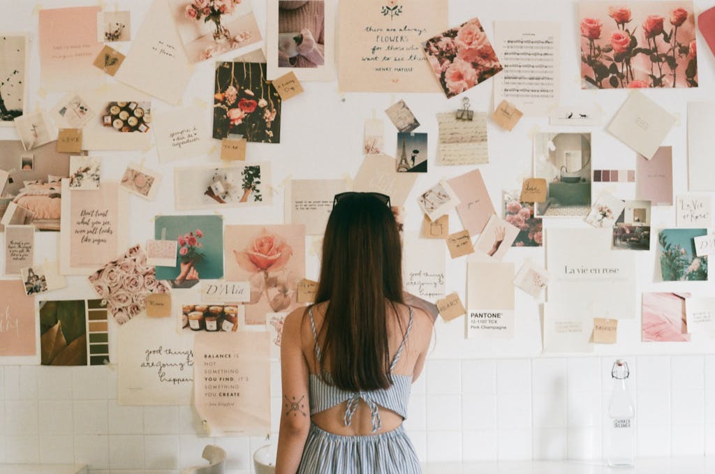 A woman with tattoos looks at a creative mood board filled with floral photos and quotes.